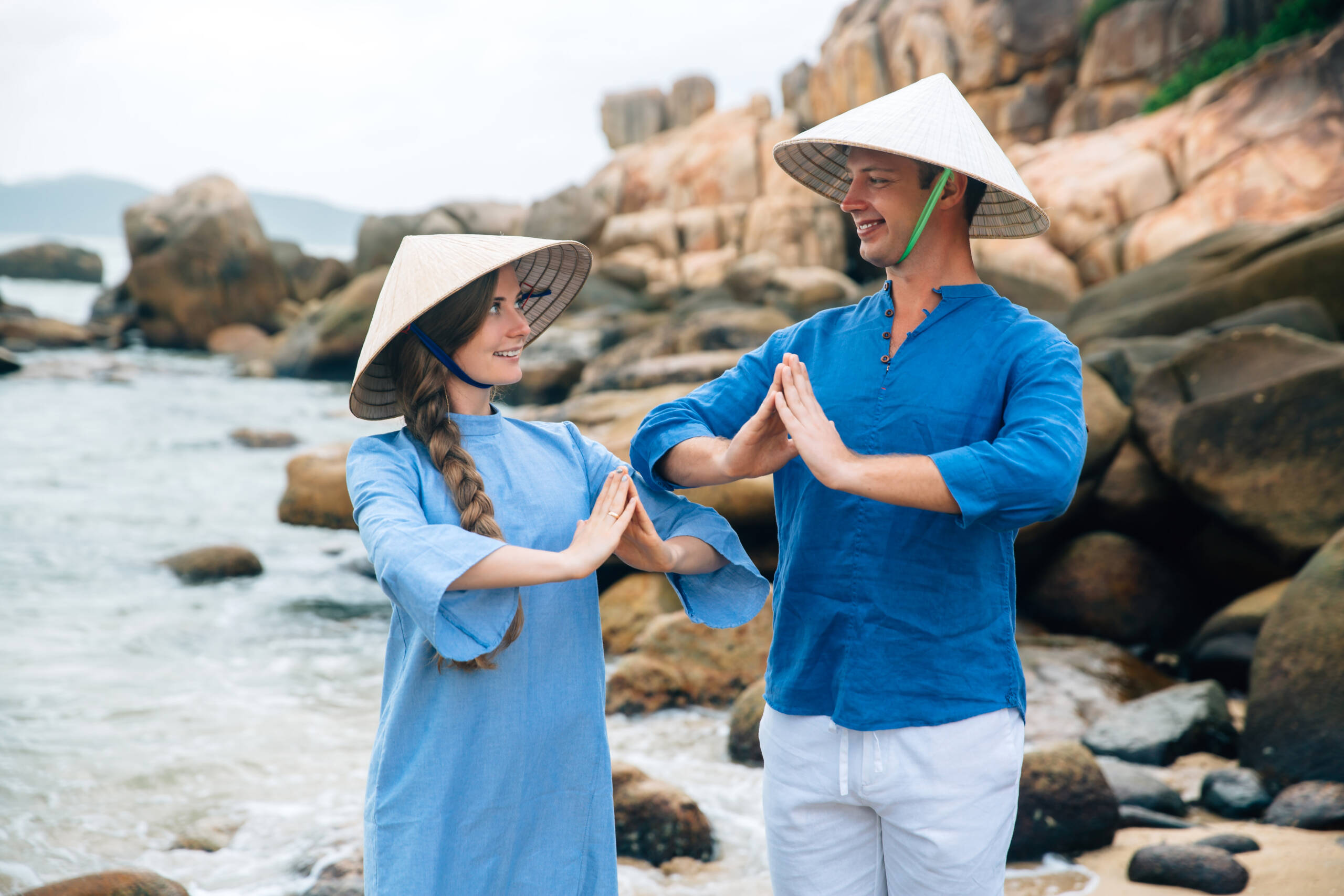 Mejor agencia para viajar a Vietnam young couple in love dressed blue shirt and Vietnamese hats in yoga pose on the beach